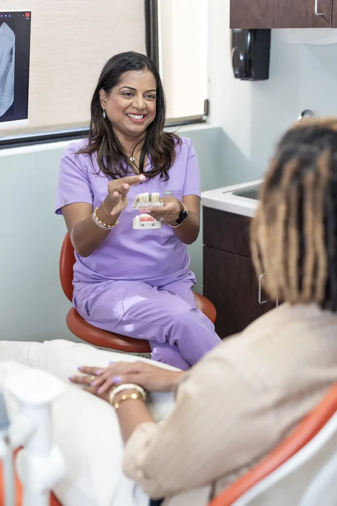 Dr. Priya Mathew holding a dental model during a consultation