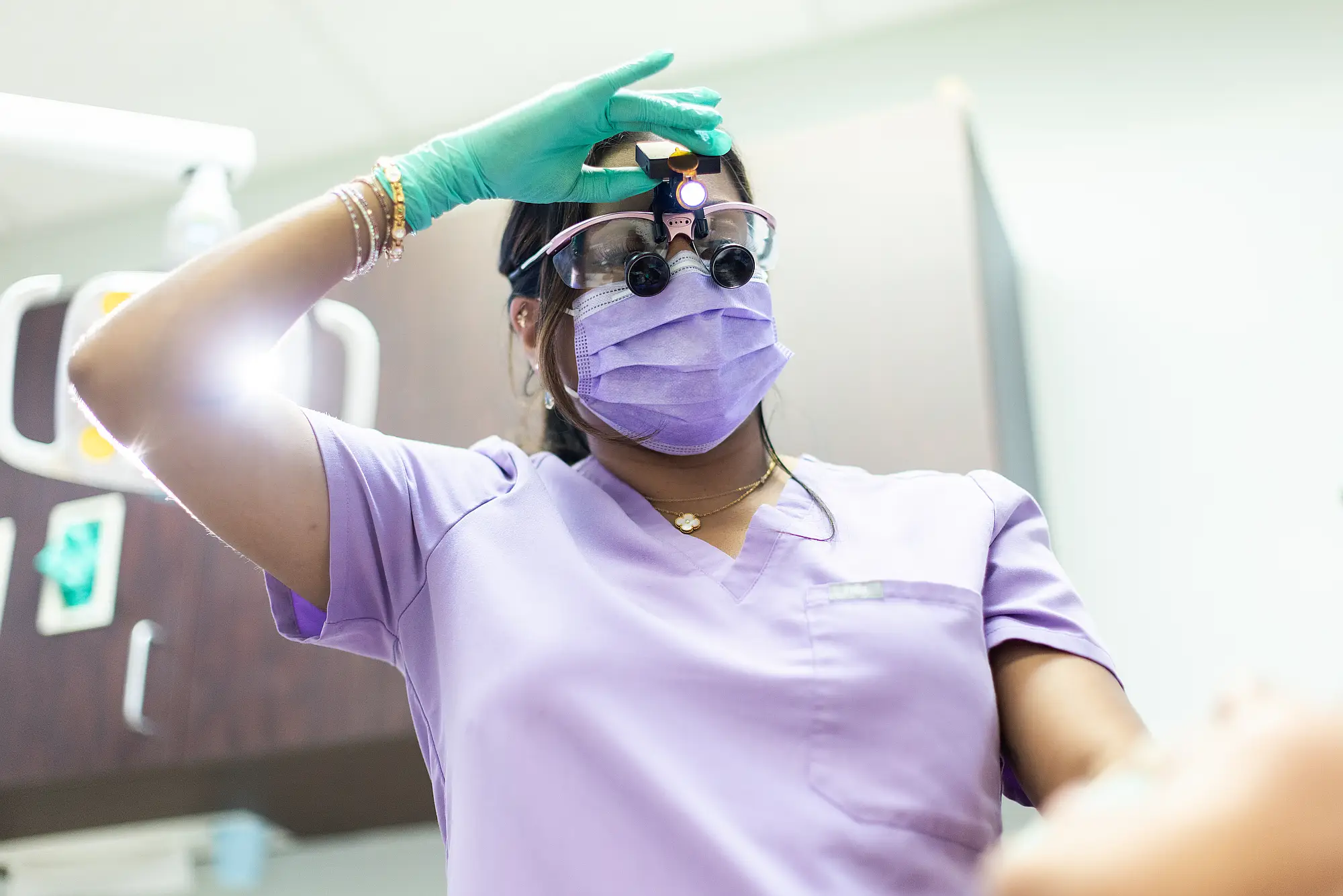 Hygienist wearing loupes and a headlamp beside a patient