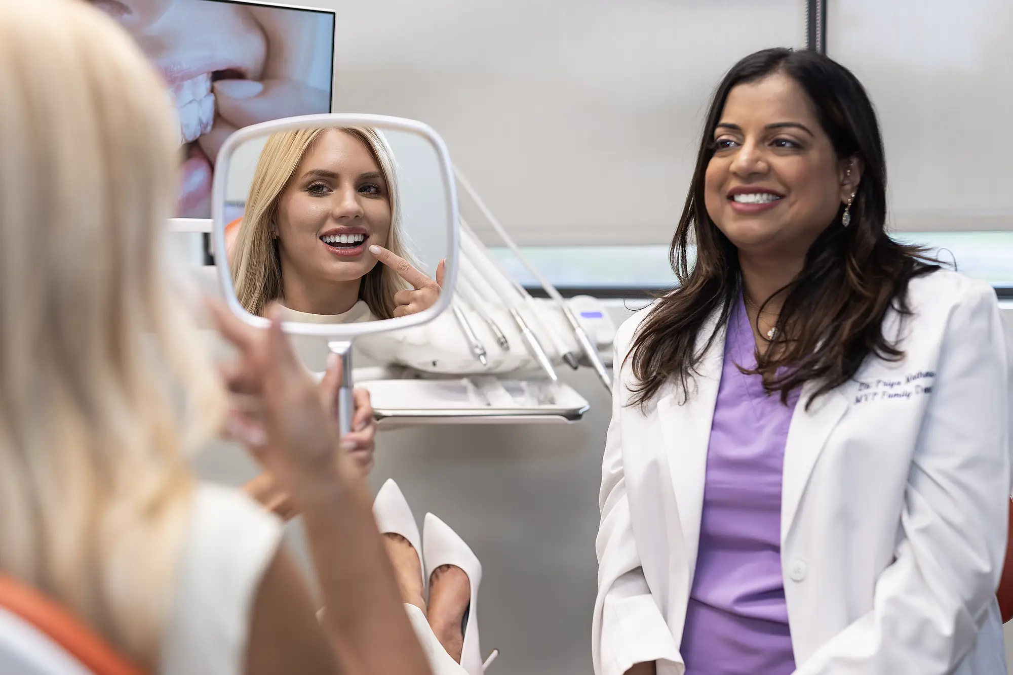 Patient looking at her smile in a mirror with Dr. Priya Mathew