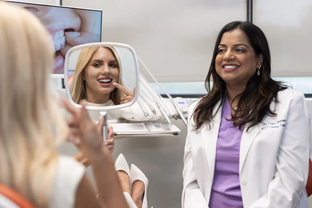 Patient and Dr. Priya Mathew looking at a smile in a hand mirror