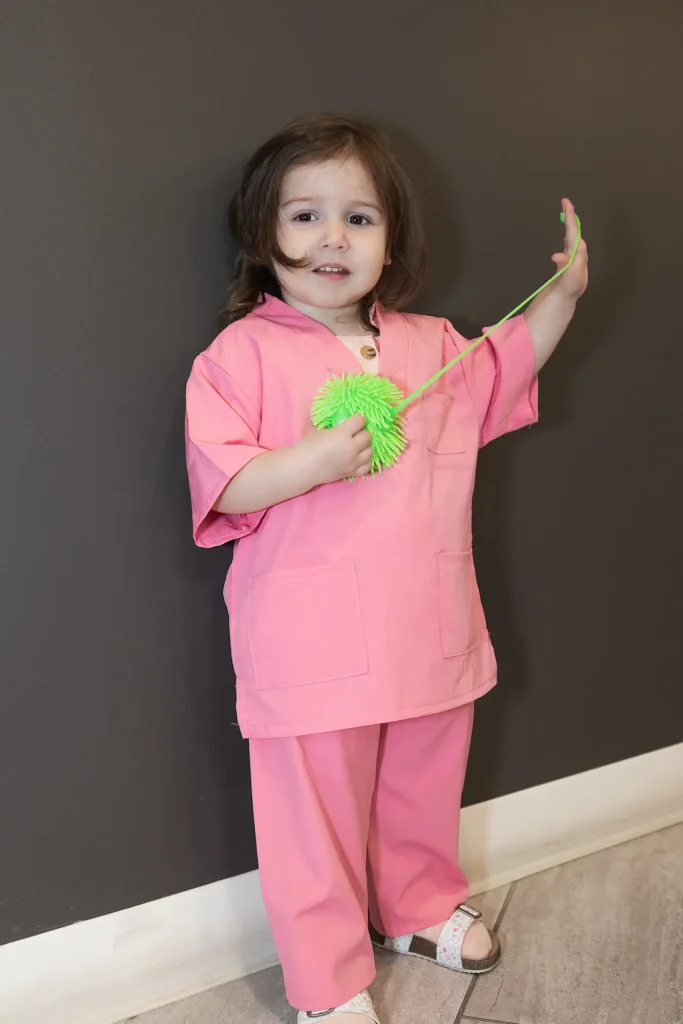 Young child in scrubs holding a toy toothbrush