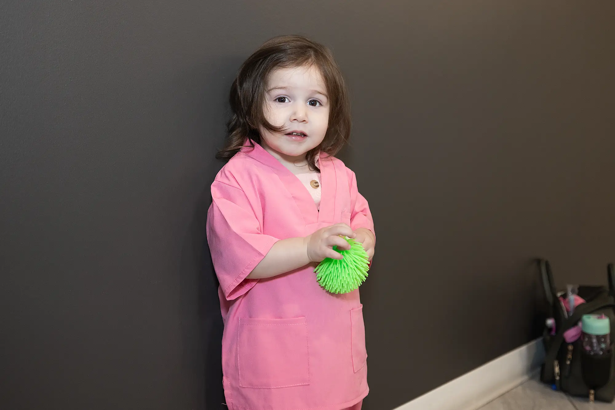 Young child in scrubs holding a green toy