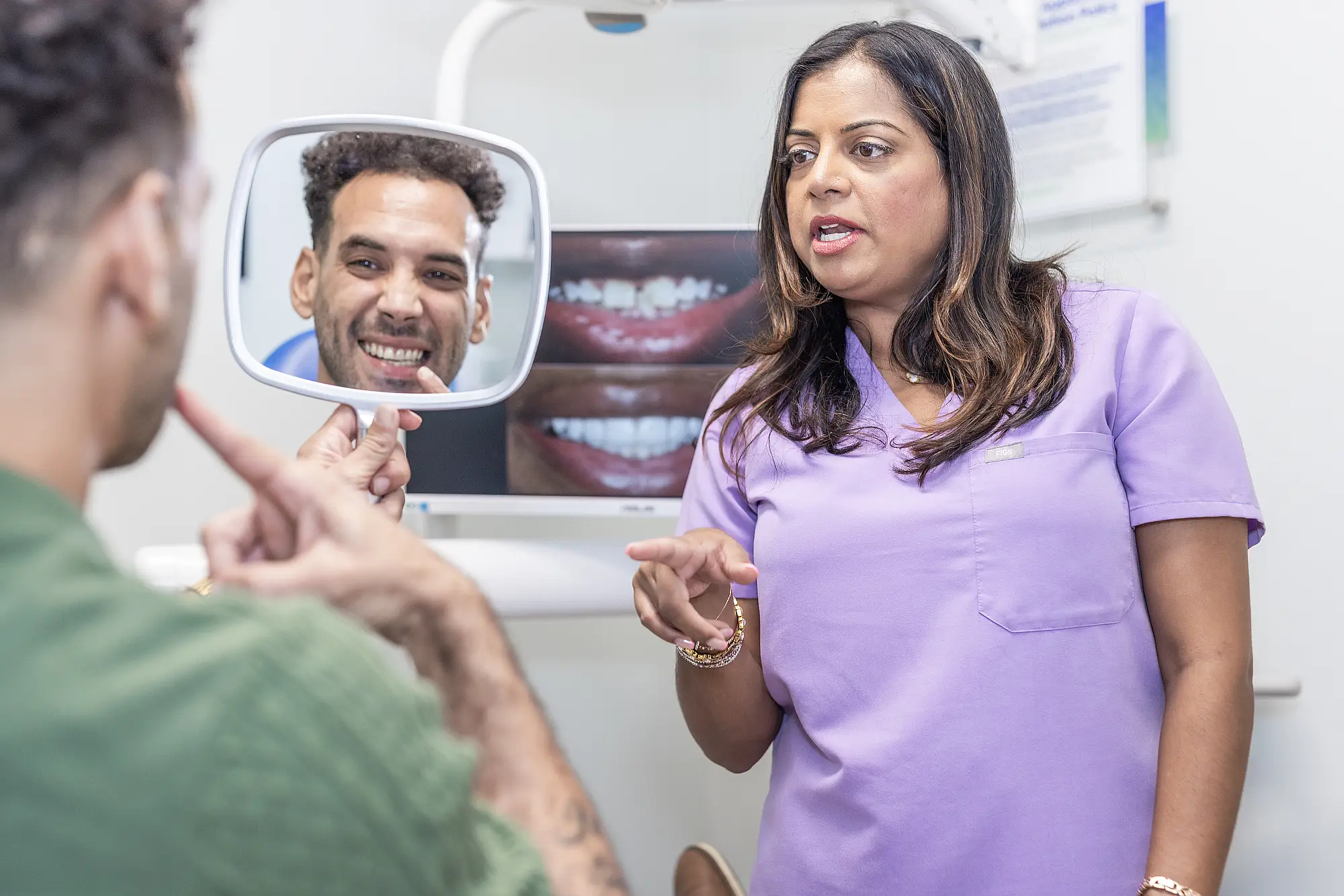 Patient looking at his smile in a hand mirror with Dr. Priya Mathew