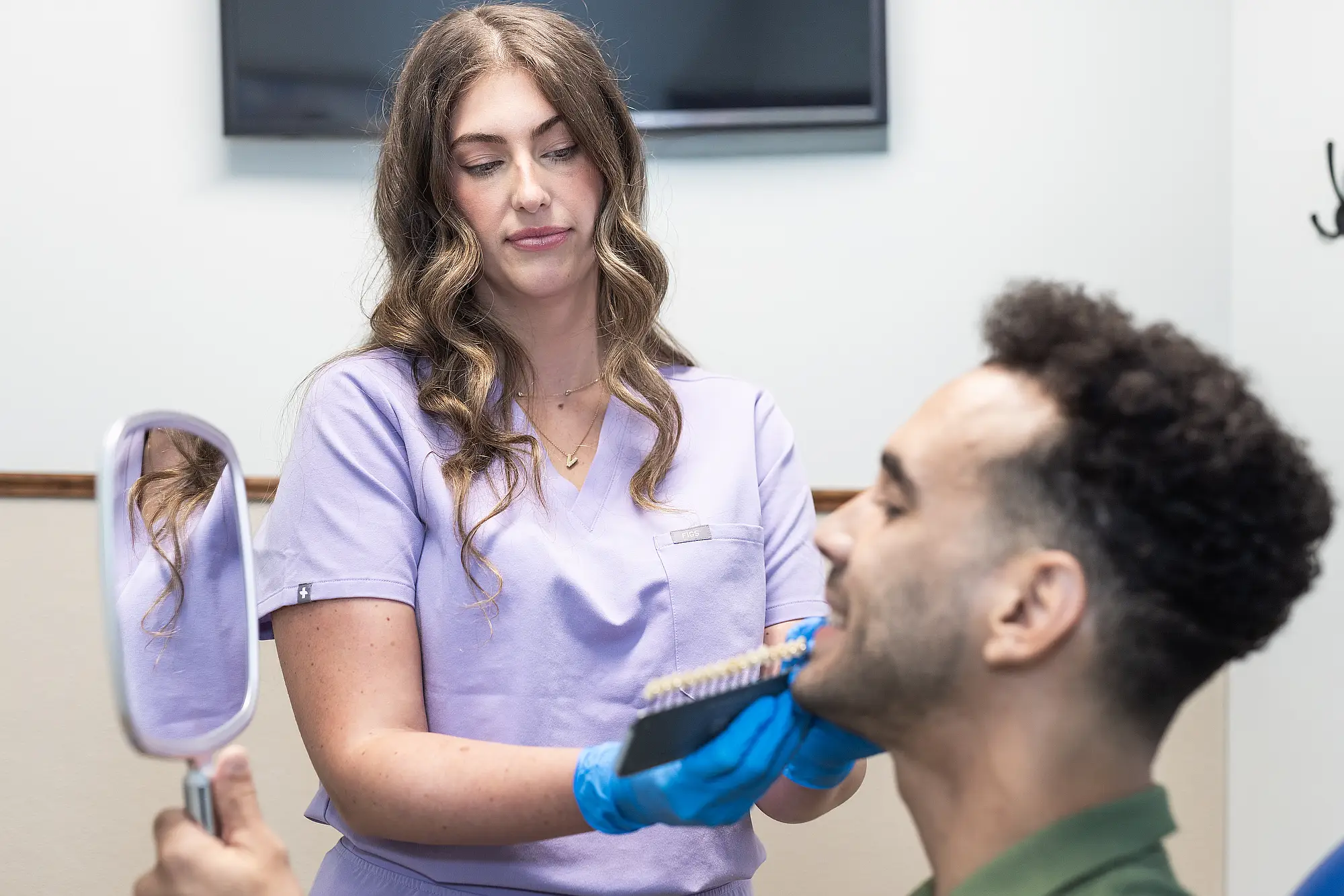 Team member holding a shade guide beside a patient's smile