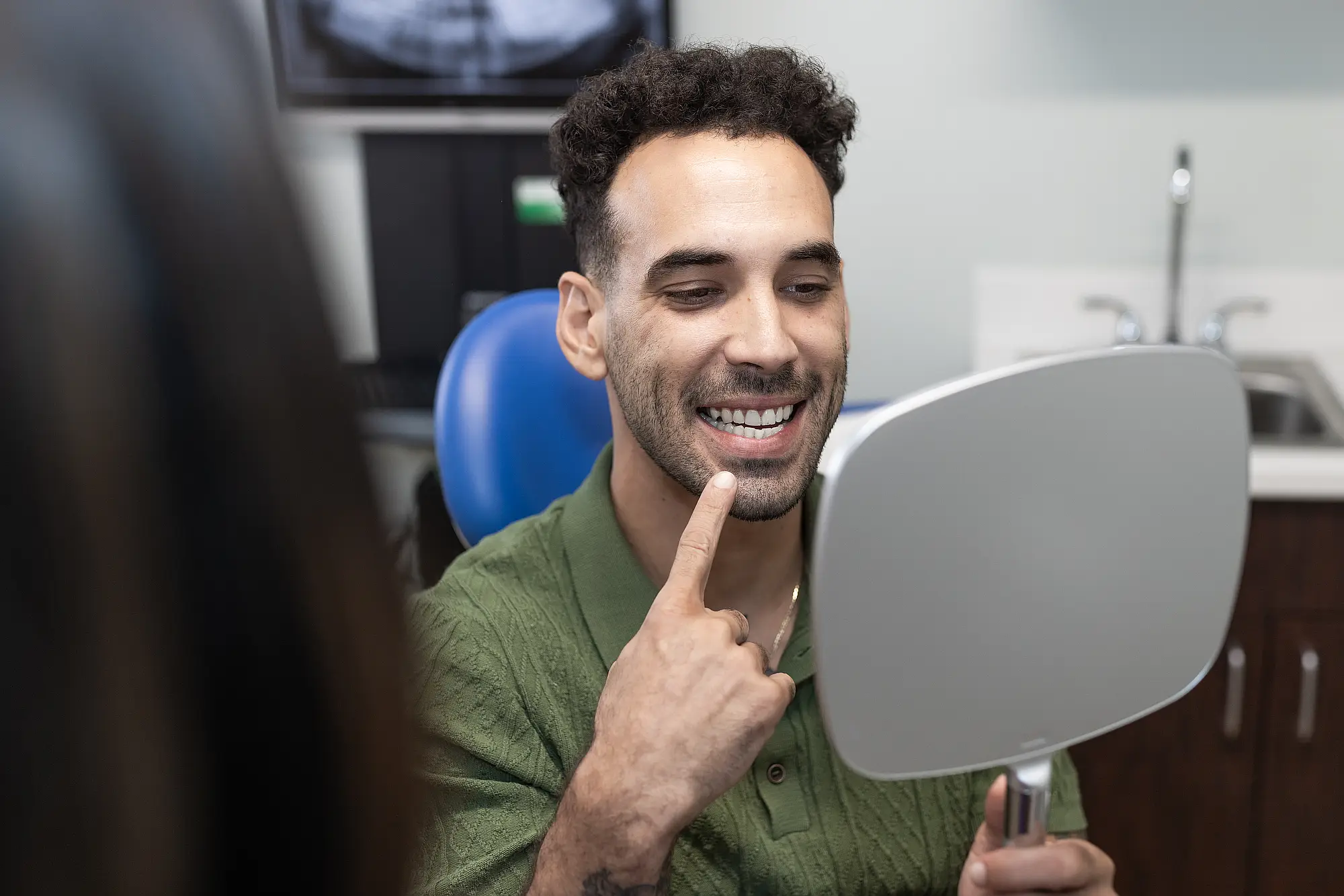 Patient pointing at his smile while holding a mirror