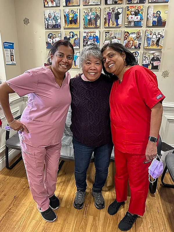 Three team members in colored scrubs with their arms around each other